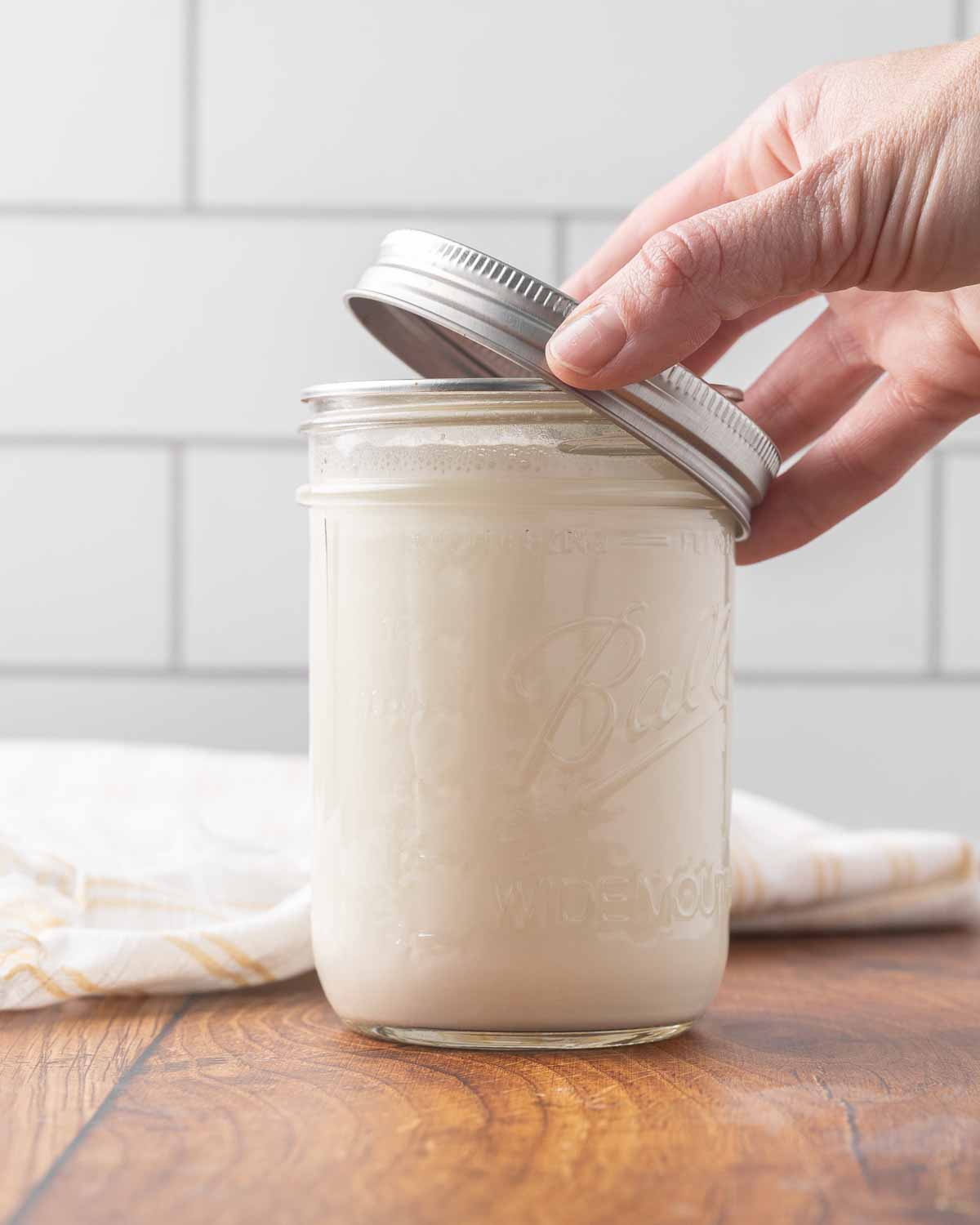 A hand placing a lid on top of a jar full of homemade yogurt.