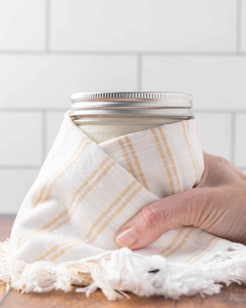A hand wrapping a jar full of milk and yogurt cultures with a towel ready to culture.