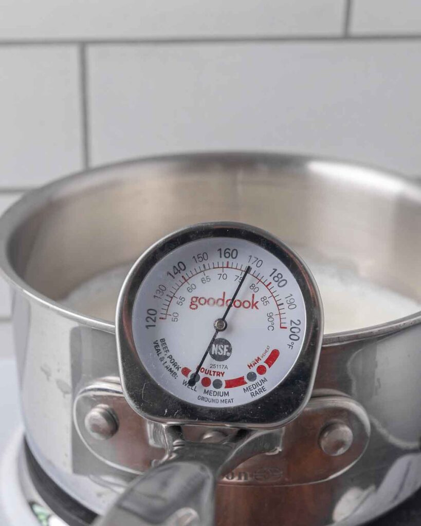 A saucepan full of milk with a thermometer showing 180&deg;F.
