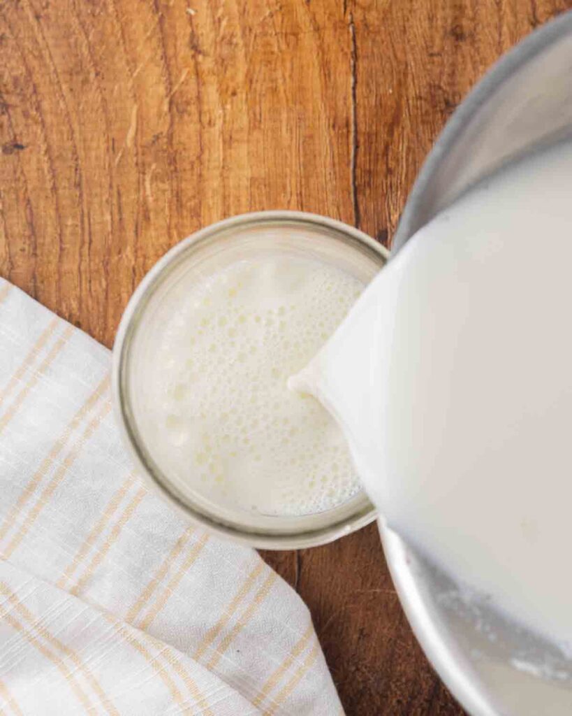 Pouring milk and culture mixture from a saucepan into a glass jar.