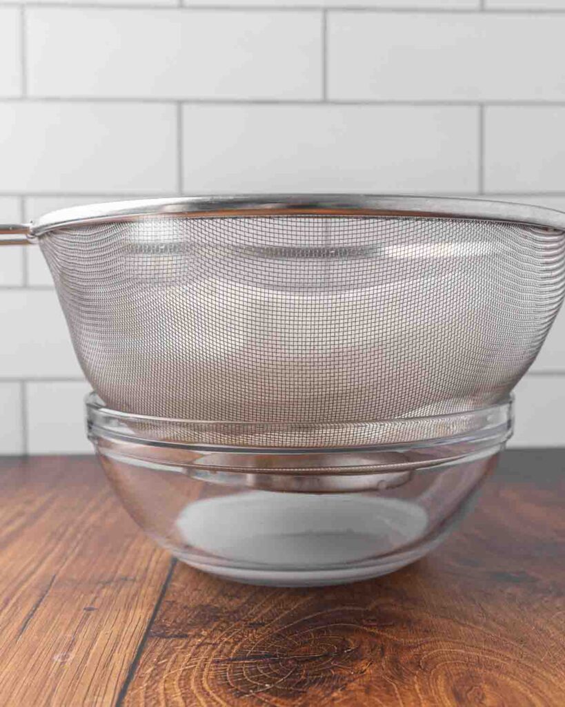 A strainer lined with cheesecloth and filled with yogurt sitting on top of a bowl to strain.