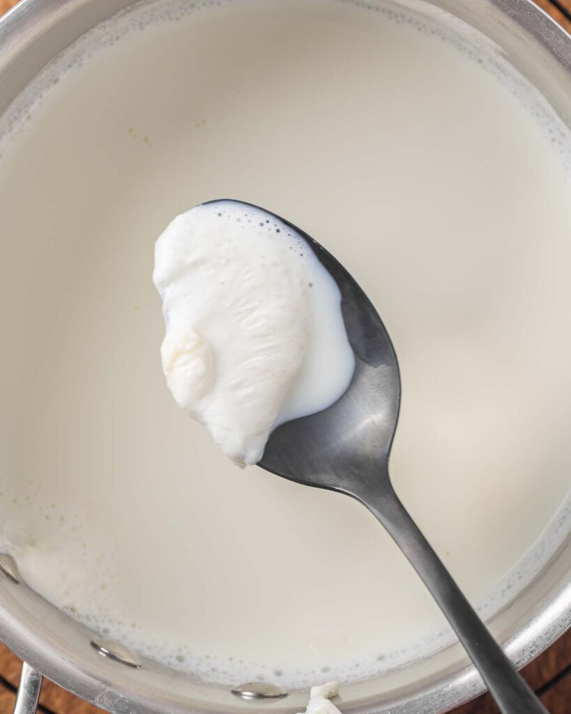 A spoon skimming off the scaled layer of heated milk.