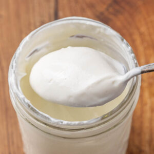 A jar of homemade Greek yogurt with a spoon lifting a bite to show texture.