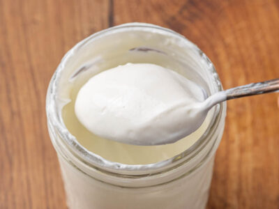 A jar of homemade Greek yogurt with a spoon lifting a bite to show texture.