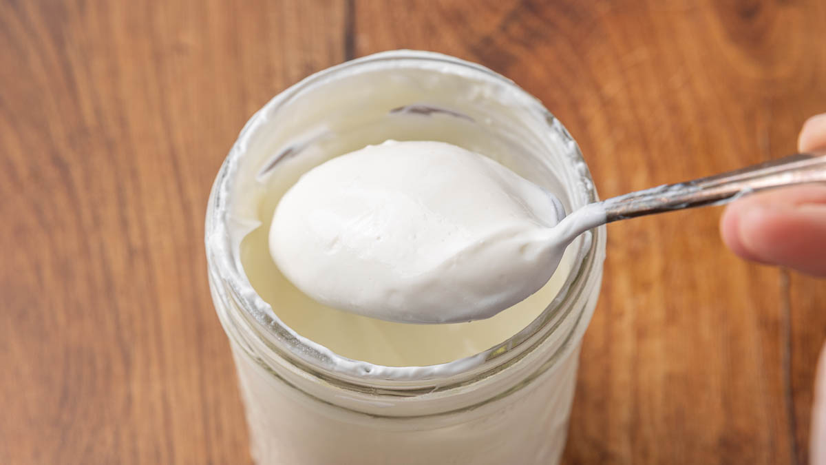 A jar of homemade Greek yogurt with a spoon lifting a bite to show texture.