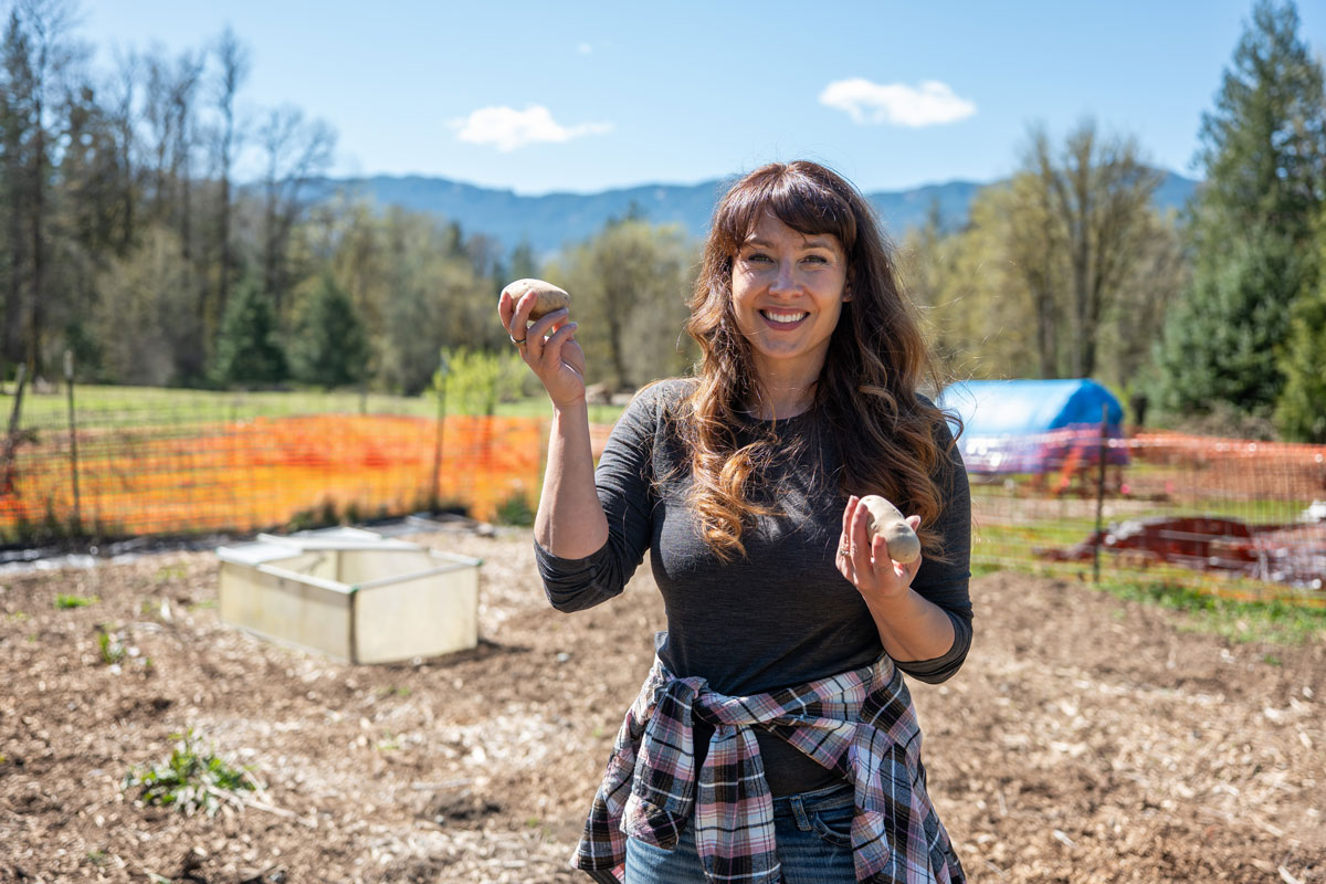 A woman holding potatoes in the garden.