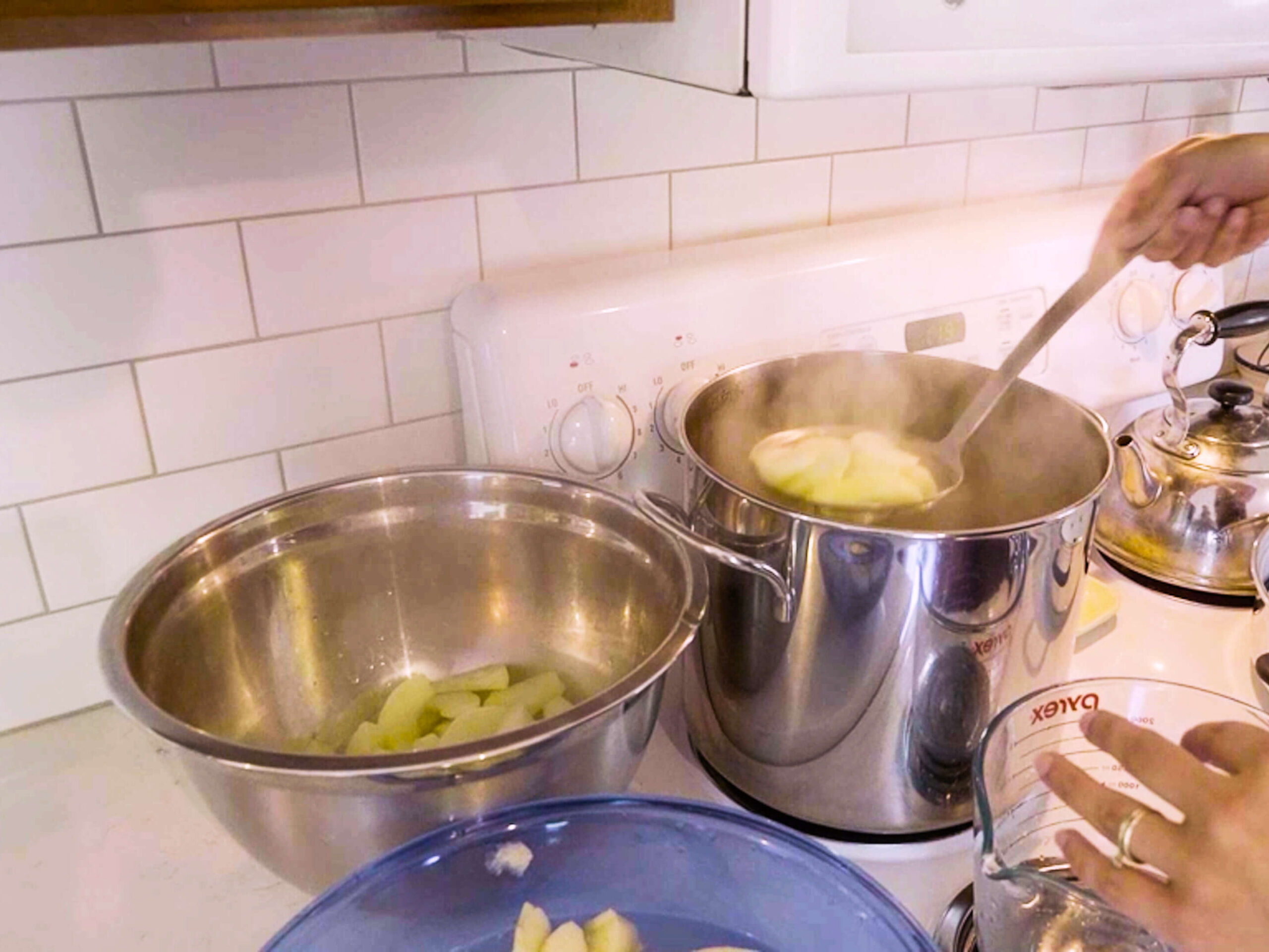 A woman removing blanched apples from a large pot on the stove.