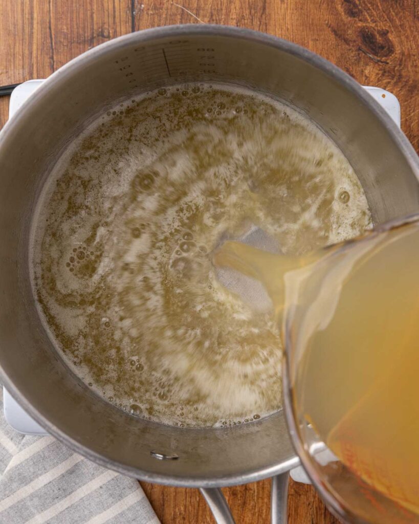 Pouring chicken into a saucepan with butter and flour mixture to make a roux. 