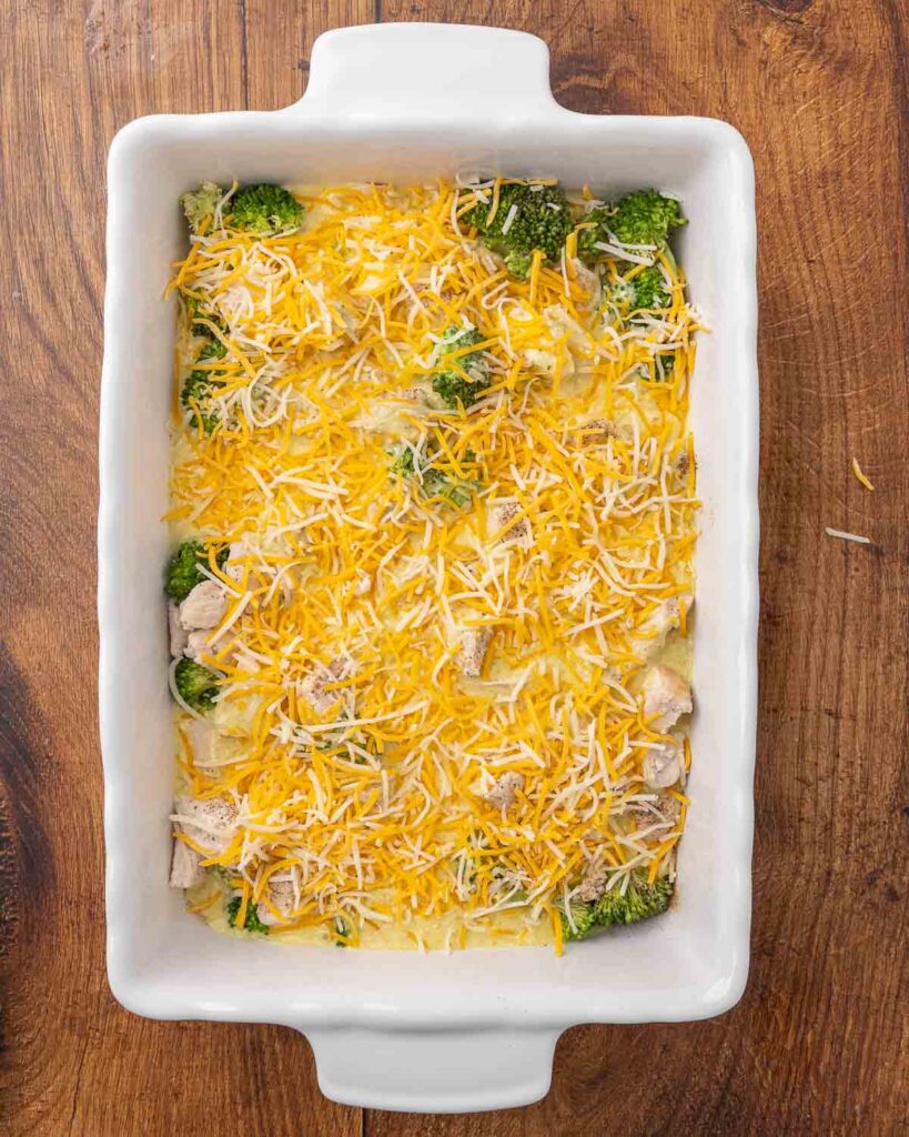 Cheddar cheese sprinkled over curry sauce, broccoli and chicken in a 9x13 pan.