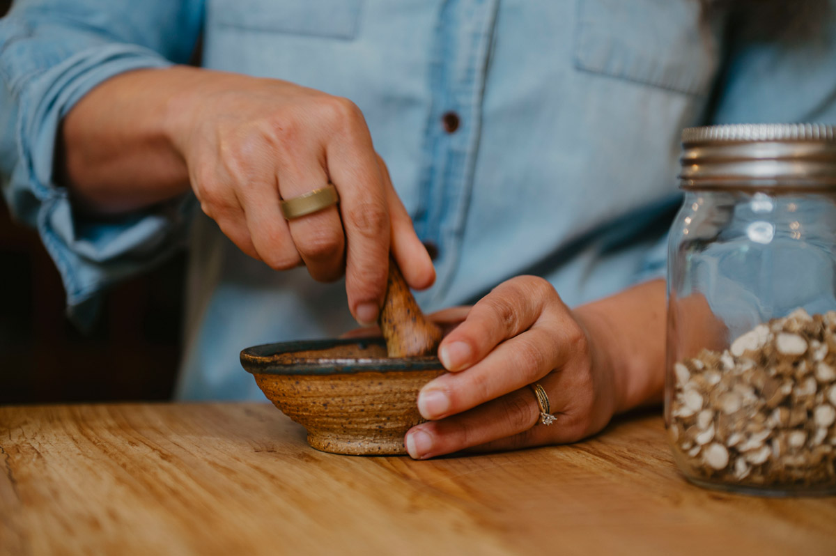 A woman crushing dried herbs with a mortar and pestle.