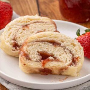 Slices of jam roly poly served on a white plate and garnished with fresh strawberries.