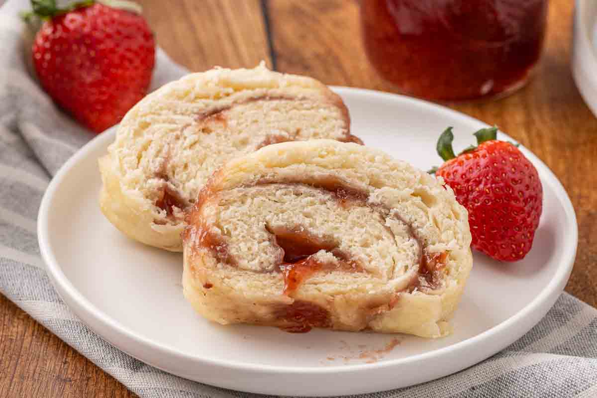 Slices of jam roly poly served on a white plate and garnished with fresh strawberries.