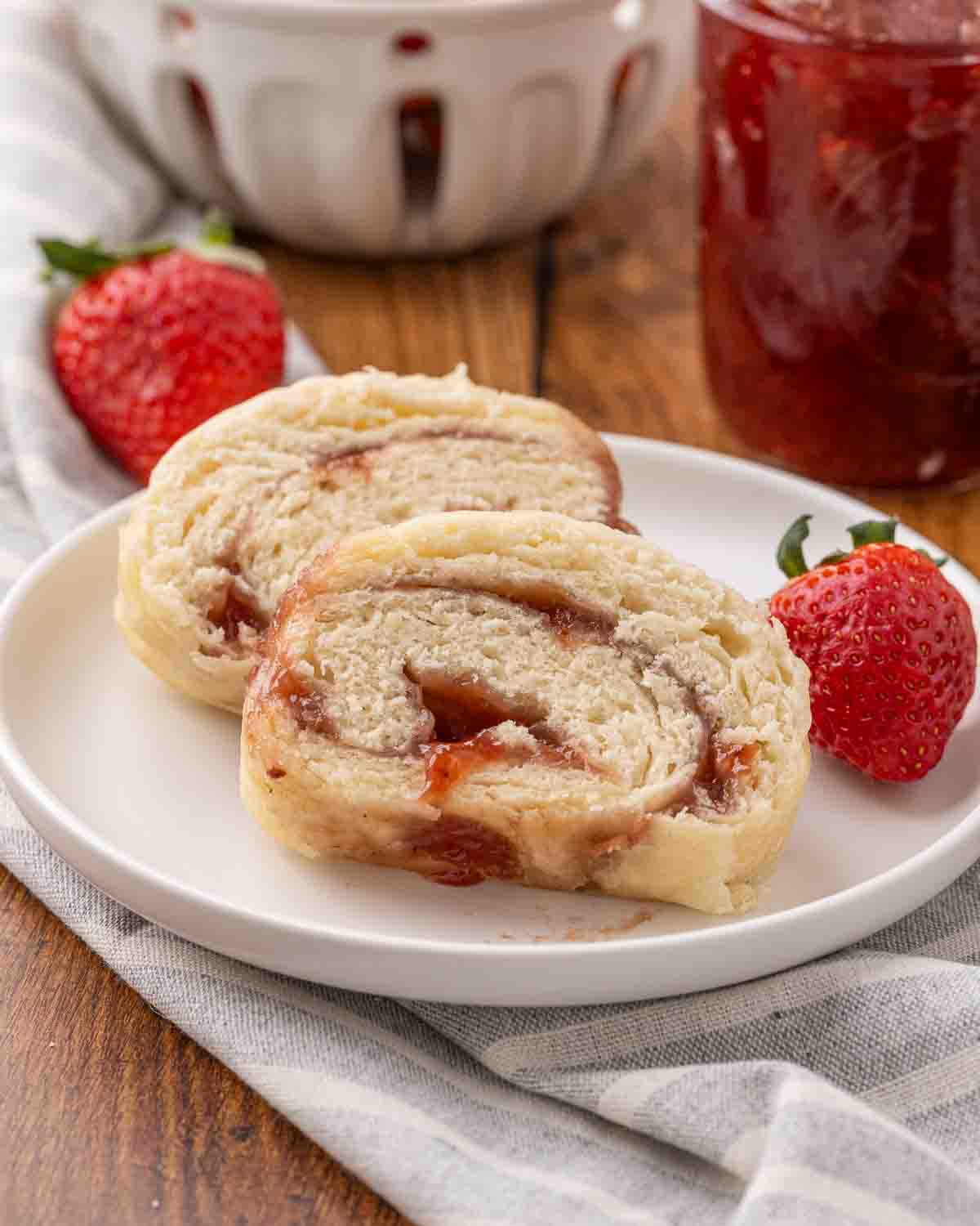 Slices of jam roly poly served on a white plate and garnished with fresh strawberries.