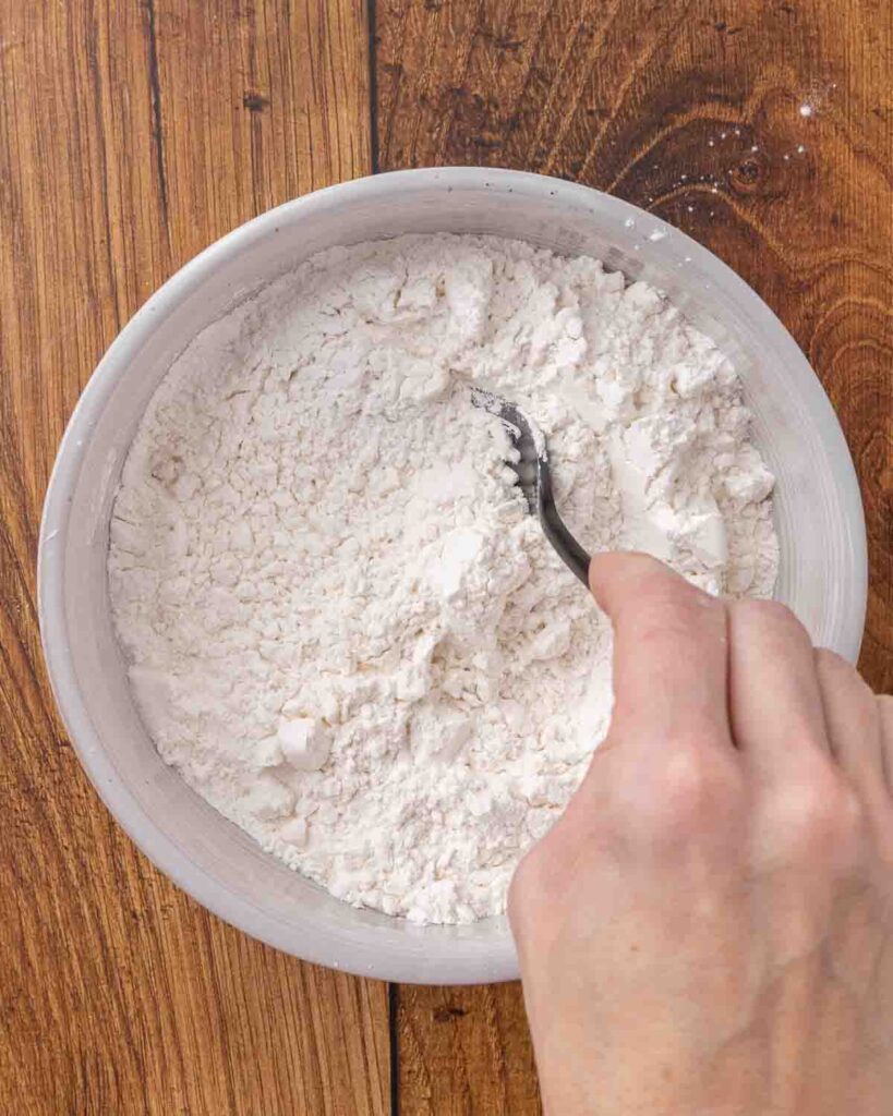 A spoon mixing jam roly poly dry ingredients in a bowl.