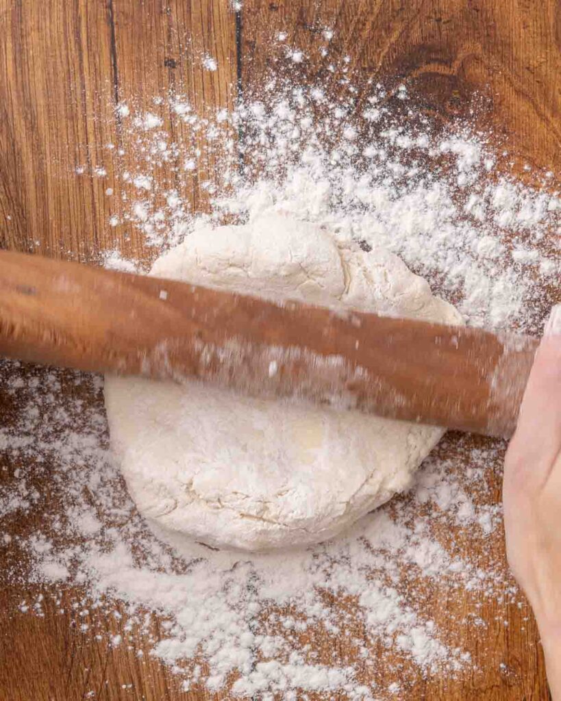 A rolling pin rolling out jam roly poly dough on a floured surface.