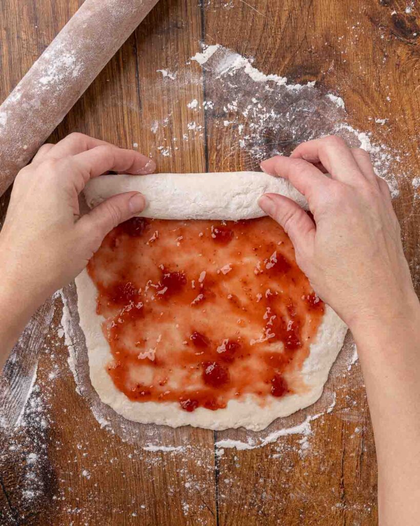 Hands rolling a jam roly poly.