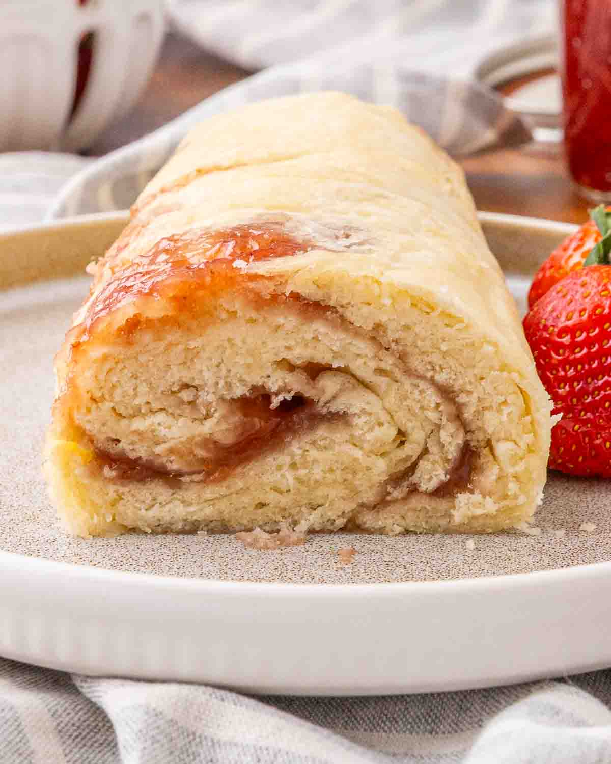 A finished jam roly poly served on a white platter and garnished with fresh strawberries.