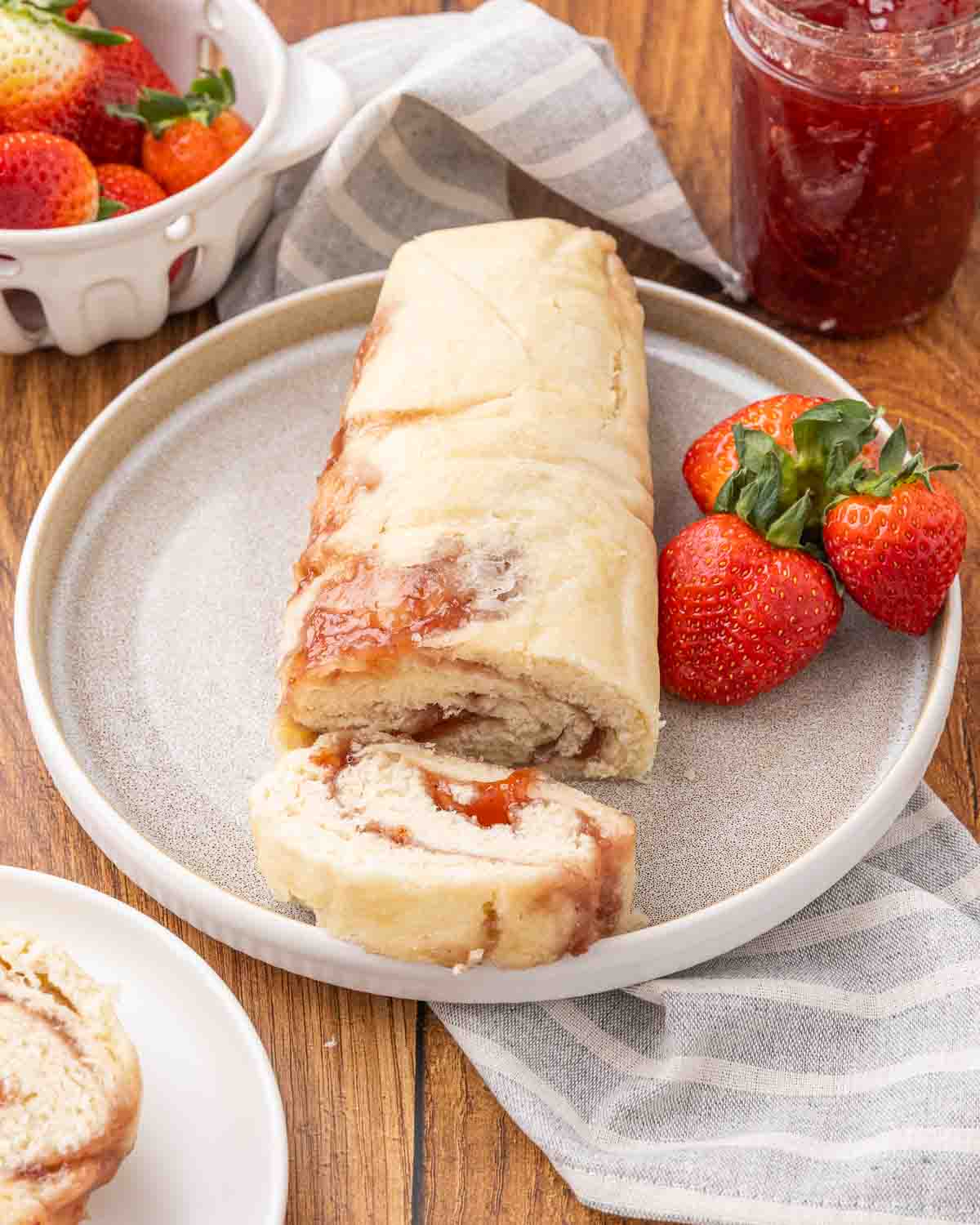 A finished jam roly poly served on a white platter and garnished with fresh strawberries.