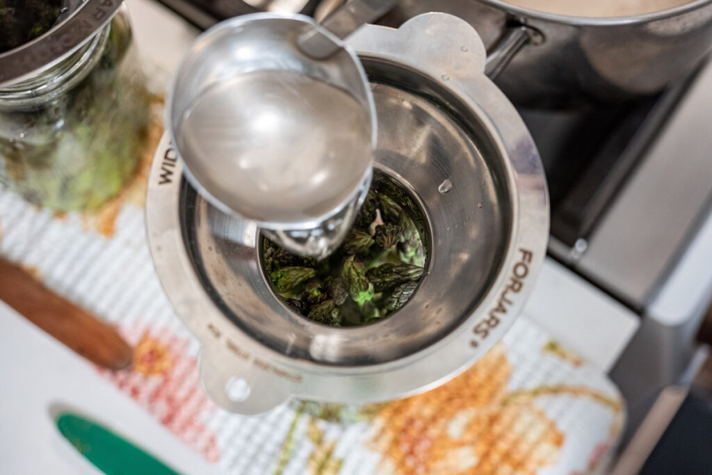 Brine being ladled into a jar of pickled asparagus.