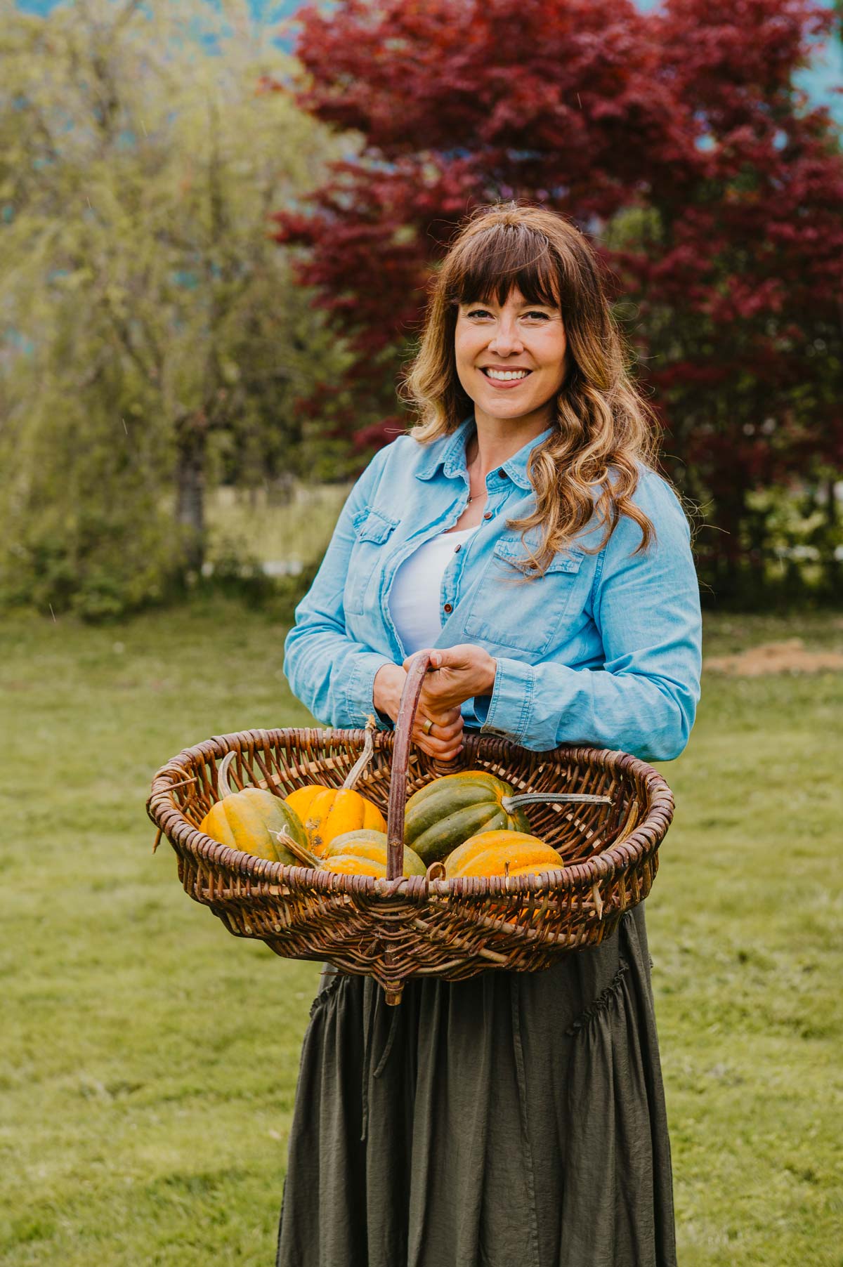A woman holding a basket filled with winter squash.