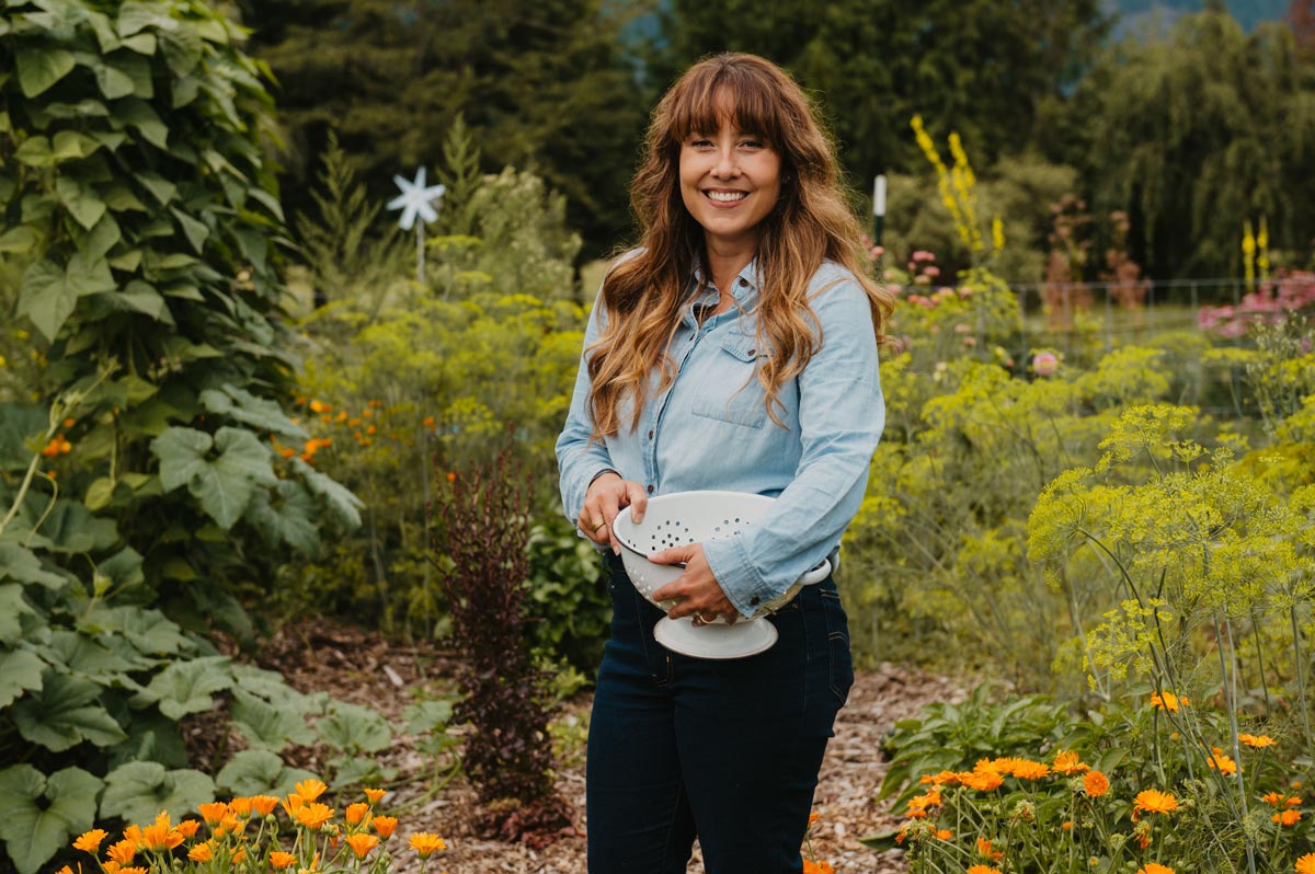 A woman holding a bowl of harvested crops in the garden.