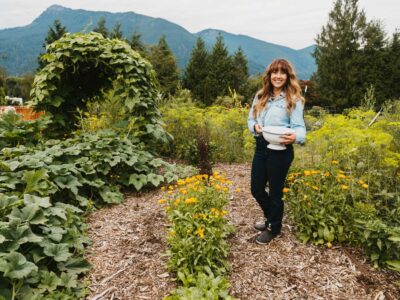 A woman holding a bowl of harvested crops in the garden.