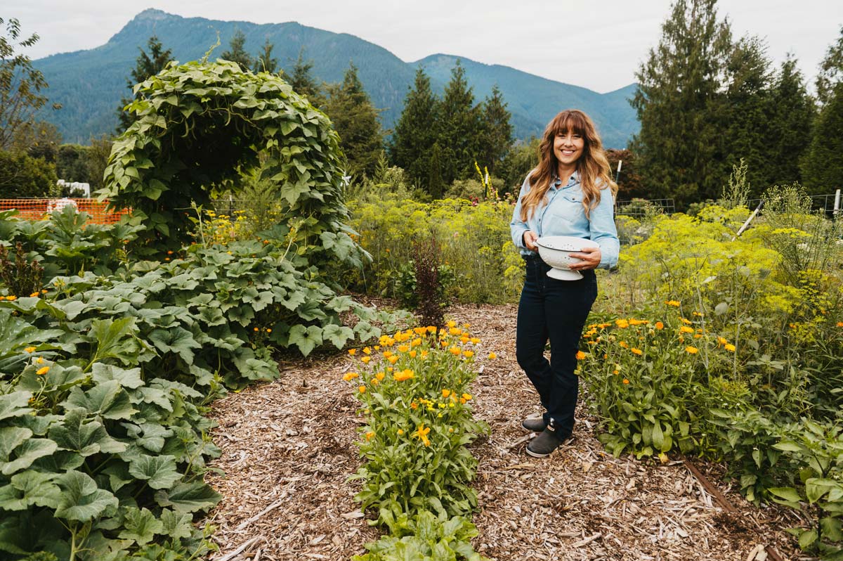 A woman holding a bowl of harvested crops in the garden.