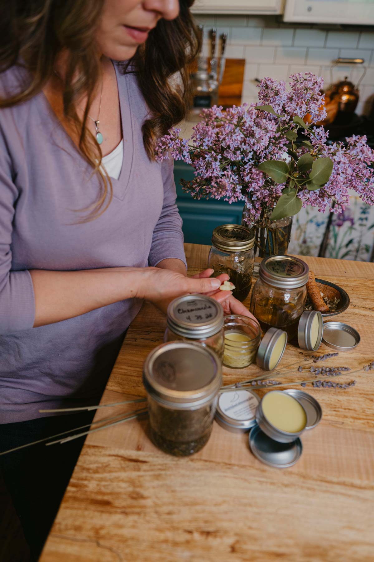 A woman with homemade herbal salves and oils on the counter.