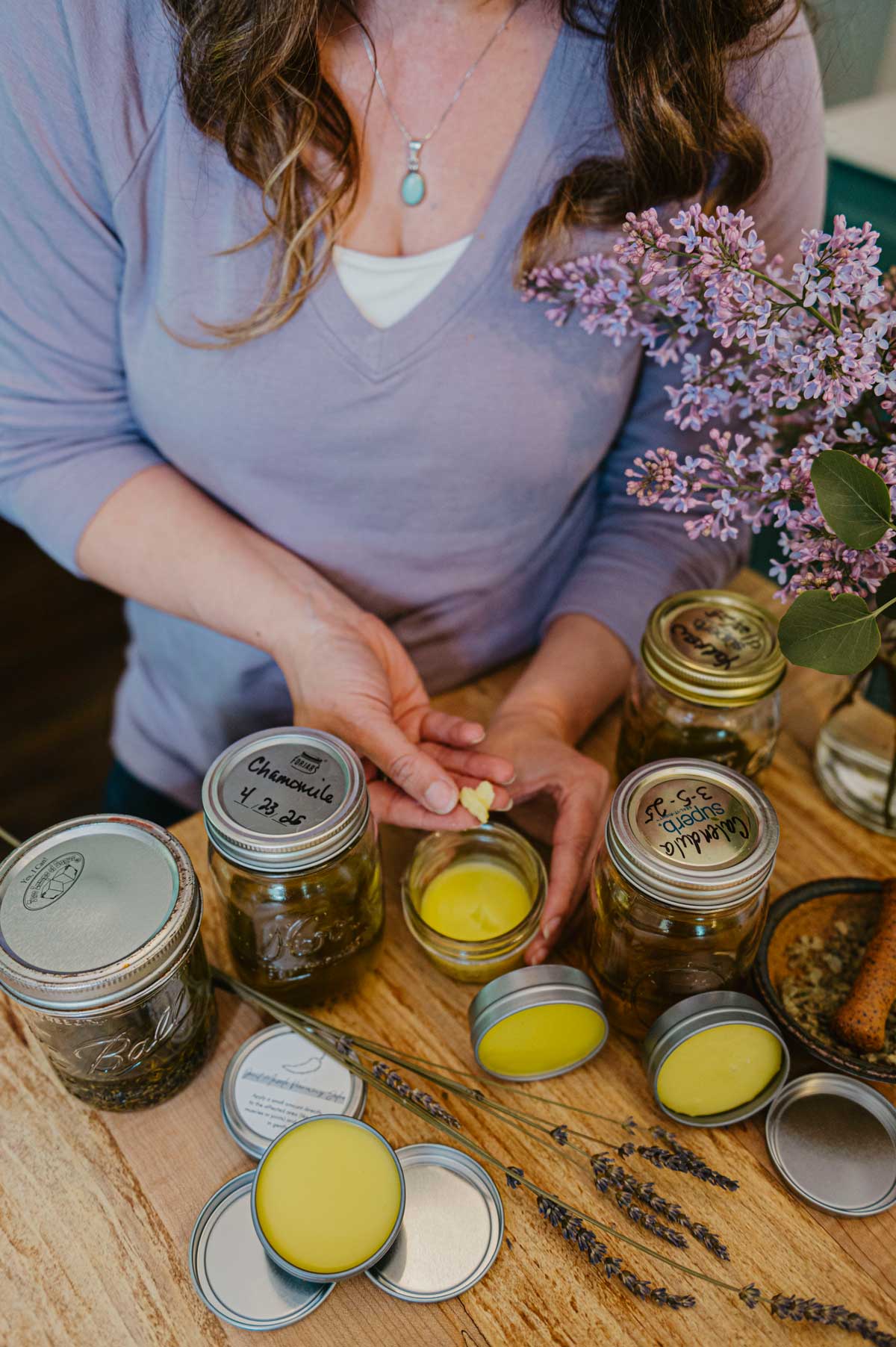 A woman with homemade herbal salves and oils on the counter.