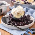 A serving of blueberry dumplings on a white plate topped with whipped cream.