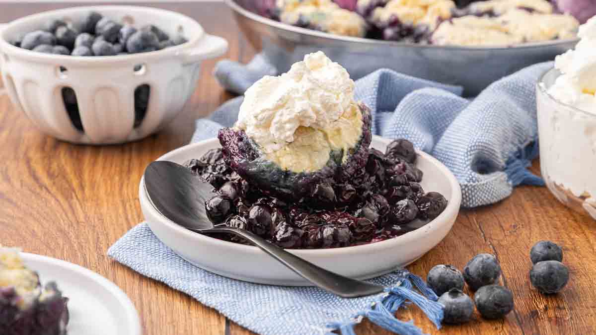 A serving of blueberry dumplings on a white plate topped with whipped cream.