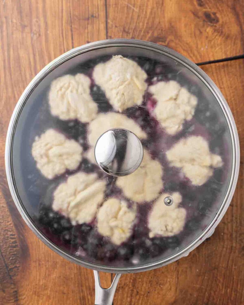 Birdseye view of a skillet filled with blueberry dumplings cooking and covered with a lid.