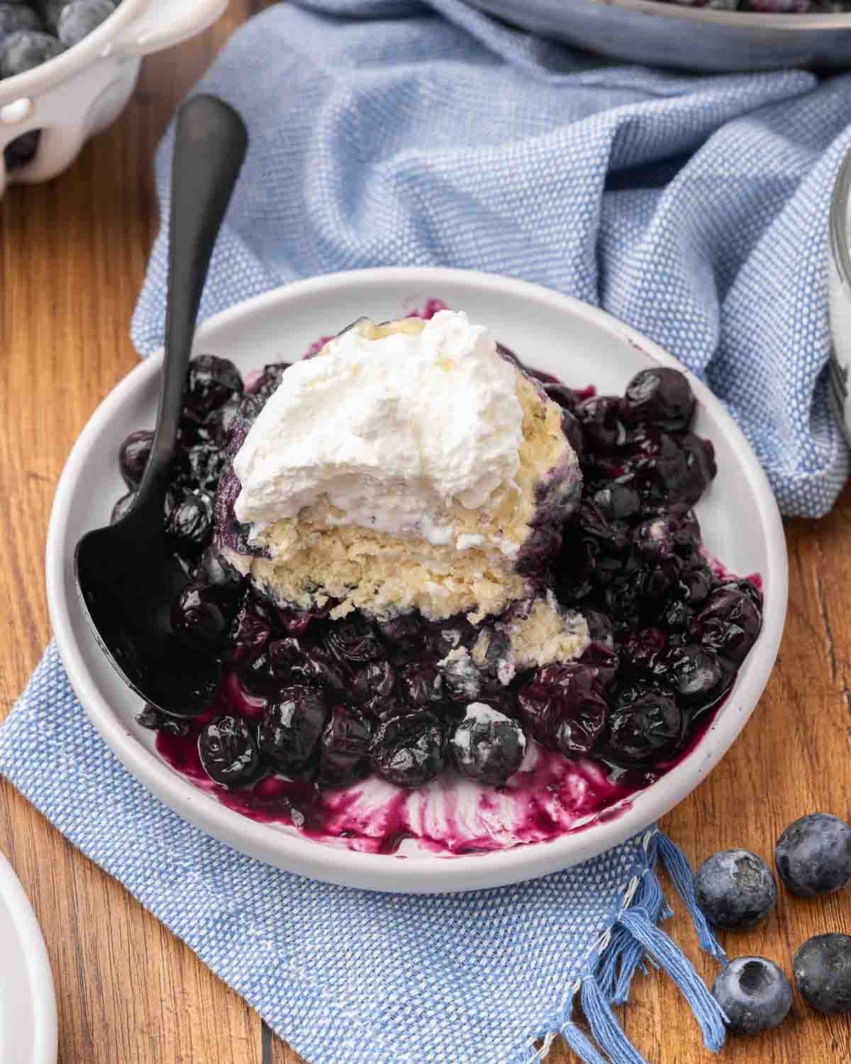 A serving of blueberry dumplings on a white plate topped with whipped cream.