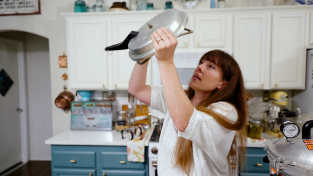 A woman inspecting the vent pipe on the lid of a pressure canner.