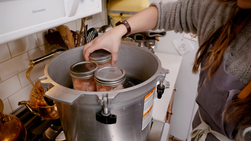 A woman placing jars of raw chicken into a pressure canner.