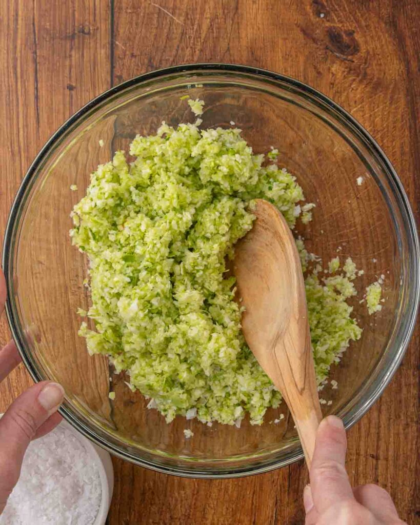 A wooden spoon mixing salt and shredded cabbage together in a bowl.