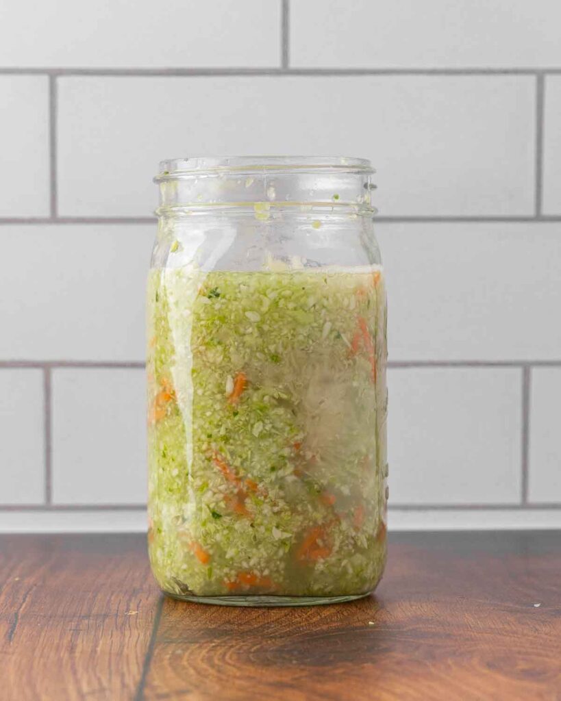 A glass jar filled with cabbage, carrots, and brine ready to ferment.