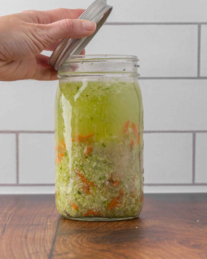 A hand placing a lid on top of a jar full of fermented sauerkraut.