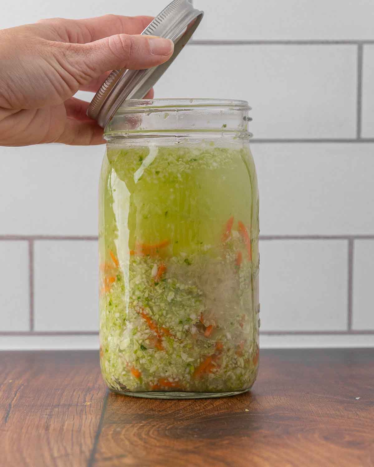 A hand placing a lid on top of a jar full of fermented sauerkraut.