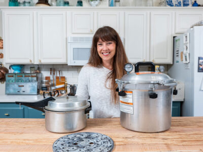 A woman standing by two pressure canners in the kitchen.