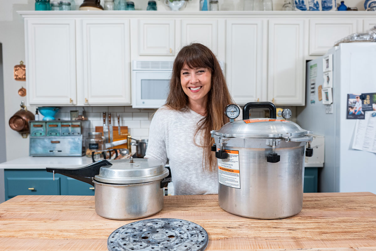 A woman standing by two pressure canners in the kitchen.