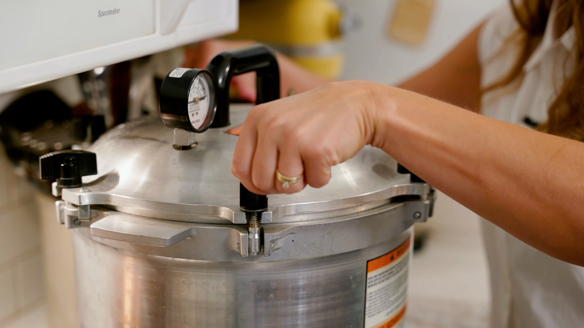A woman tightening the latches on the lid of a pressure canner.