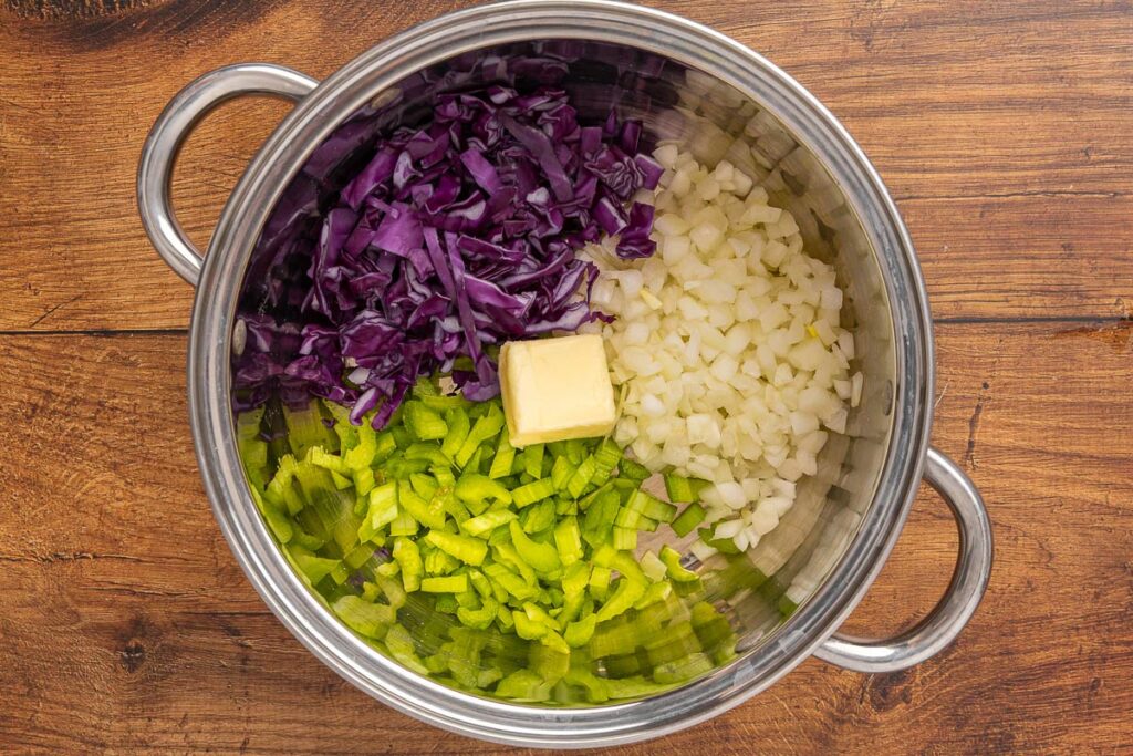 A bird's eye view of diced onions, celery, cabbage, and butter in a saucepan.