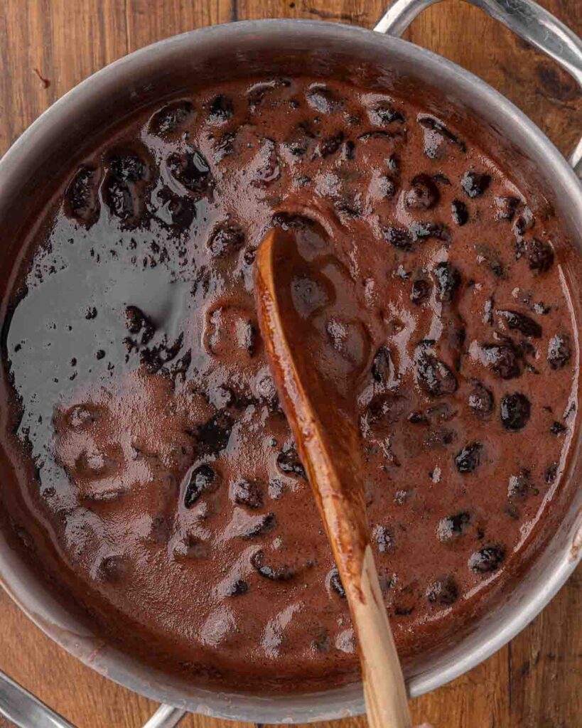 A spoon skimming the foam off of cooked chocolate cherry sauce.