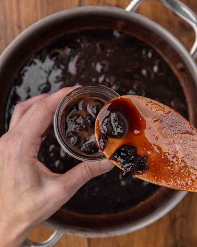 A spoon filling a jar full of chocolate cherry sauce.