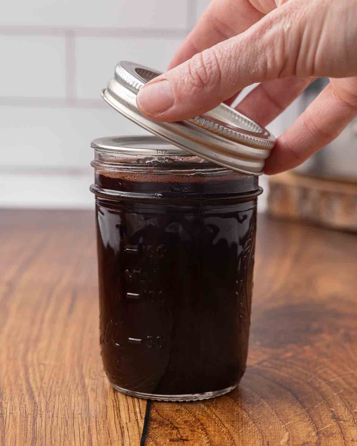 A hand placing a lid on top of a jar full of chocolate cherry sauce.