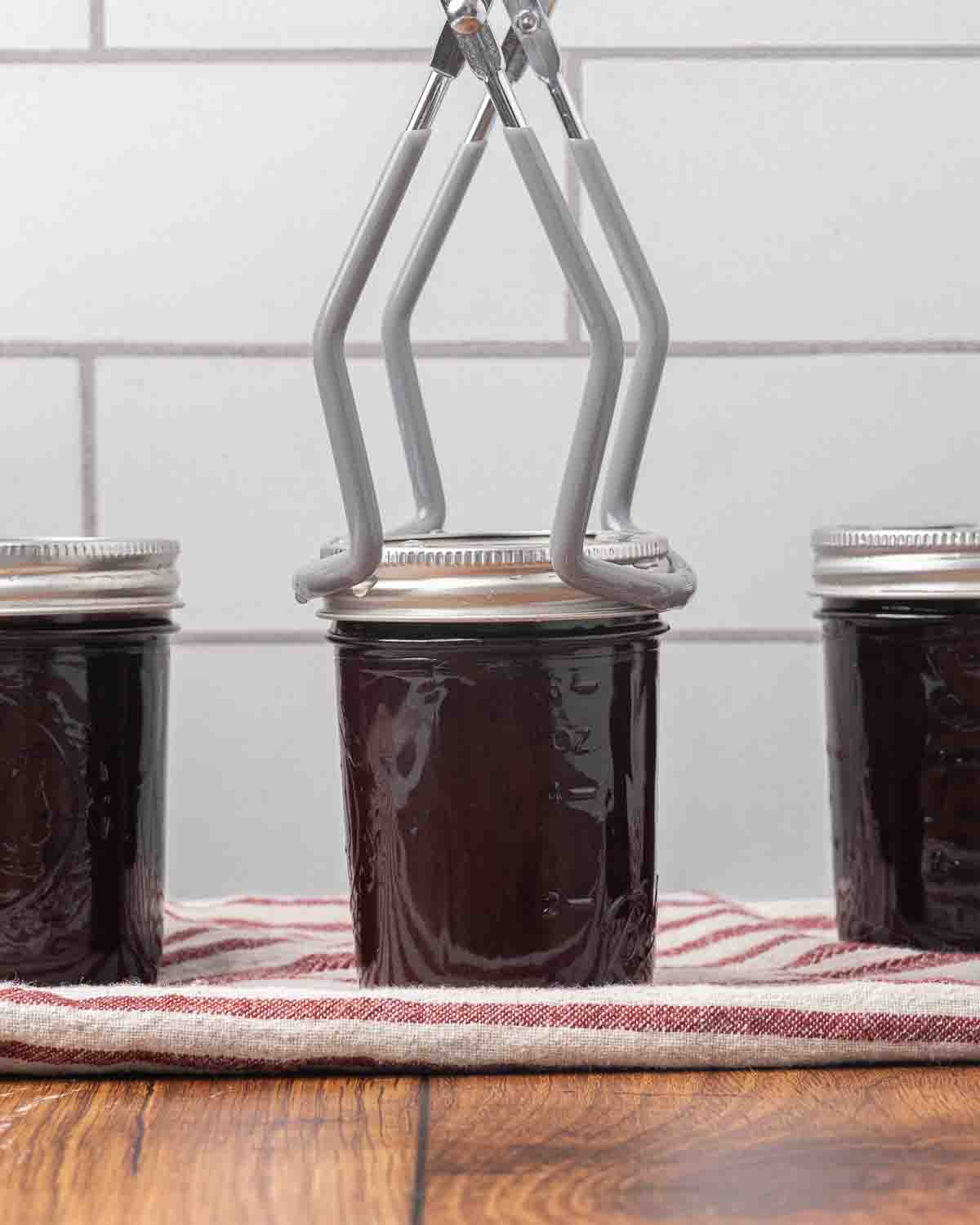 A jar lifter holding a jar of finished chocolate cherry sauce.