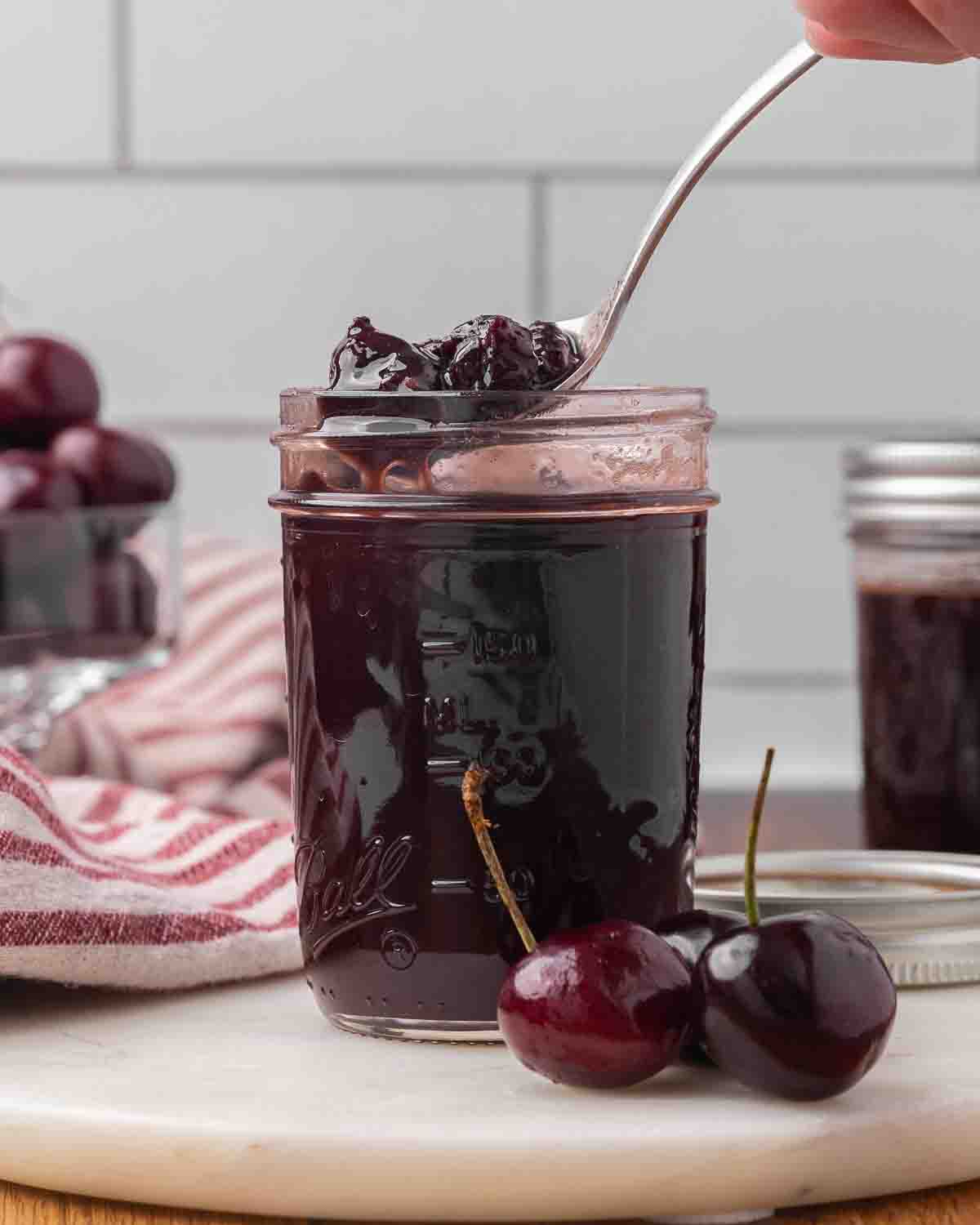 A spoon lifting chocolate cherry sauce out of a jar to show texture.