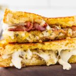 A pesto grilled cheese sandwich sliced in half and stacked on a cutting board to show the filling inside.