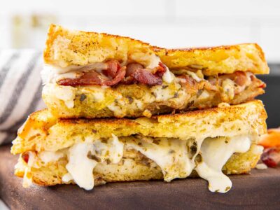 A pesto grilled cheese sandwich sliced in half and stacked on a cutting board to show the filling inside.